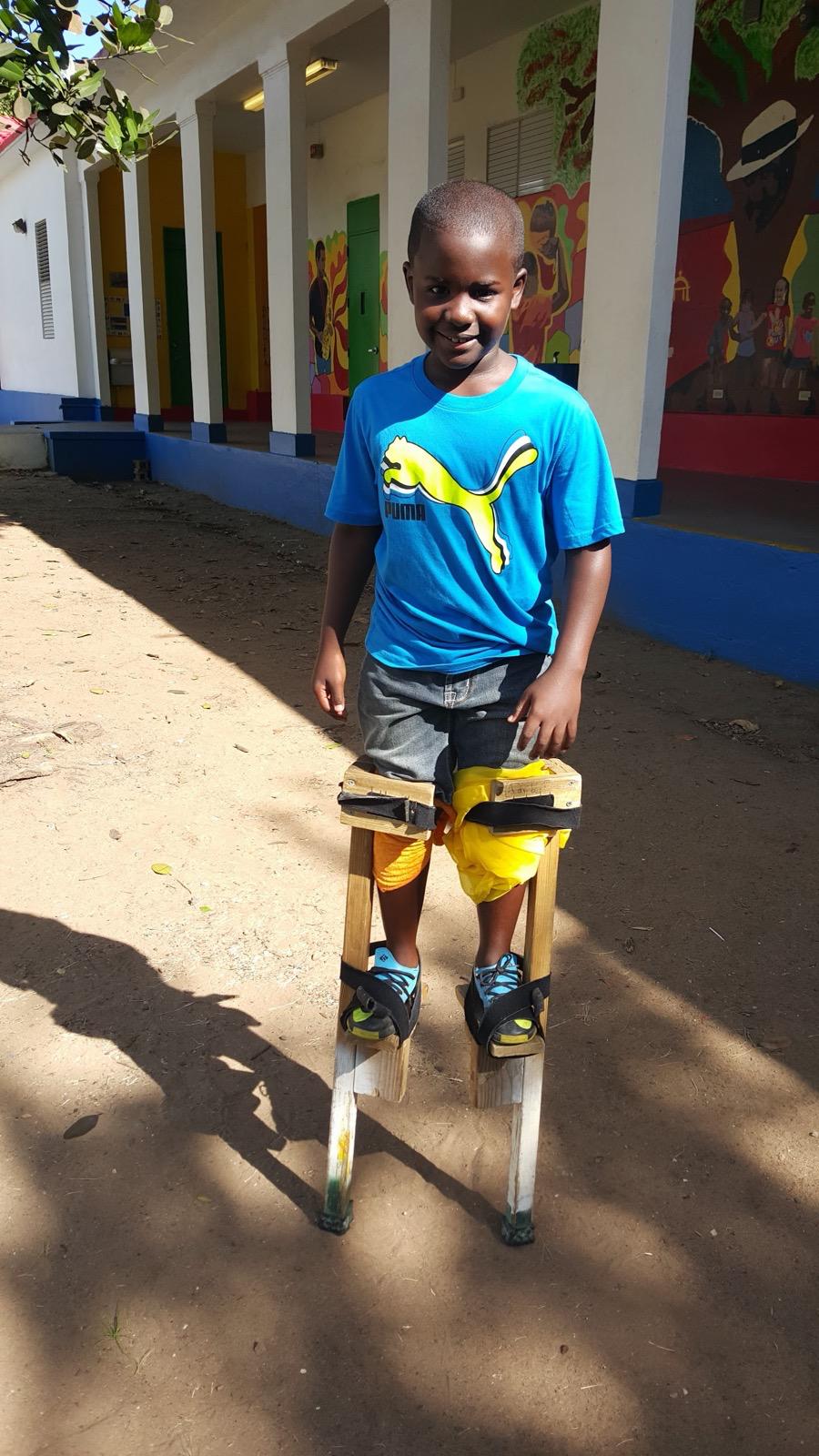 Niño aprendiendo a caminar en zancos tradicionales con una sonrisa orgullosa